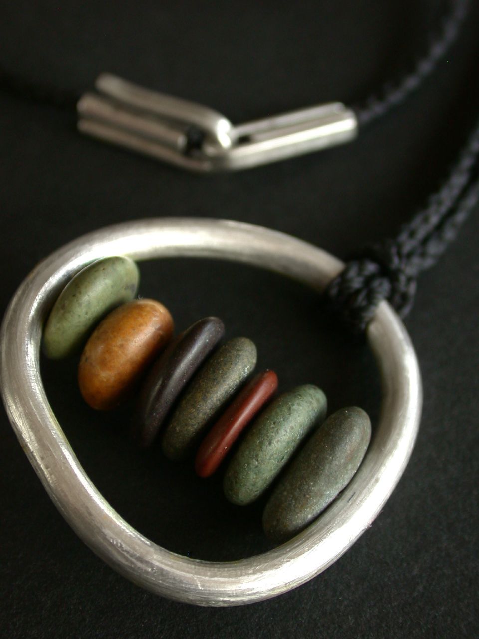 Sterling silver loop pendant holding six river pebbles on waxed black cord